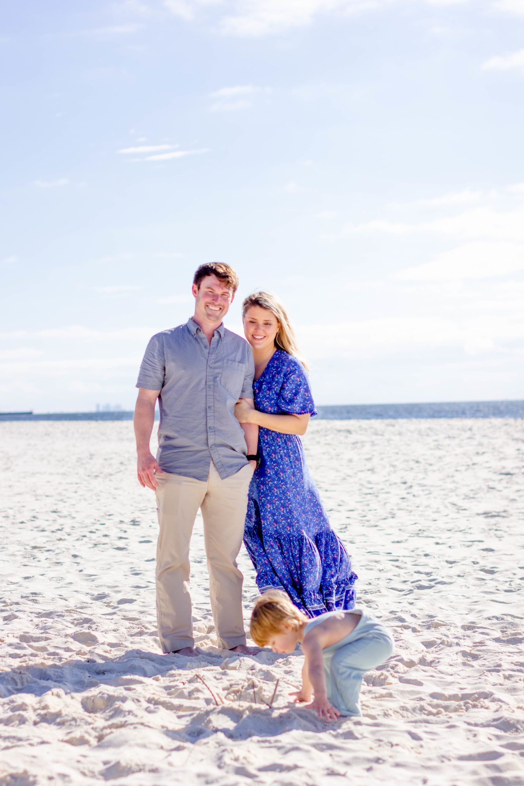 A couple on the beach watching their son before sunset in Pensacola, FL during a family beach mini photo session by Jenny Macy Photography