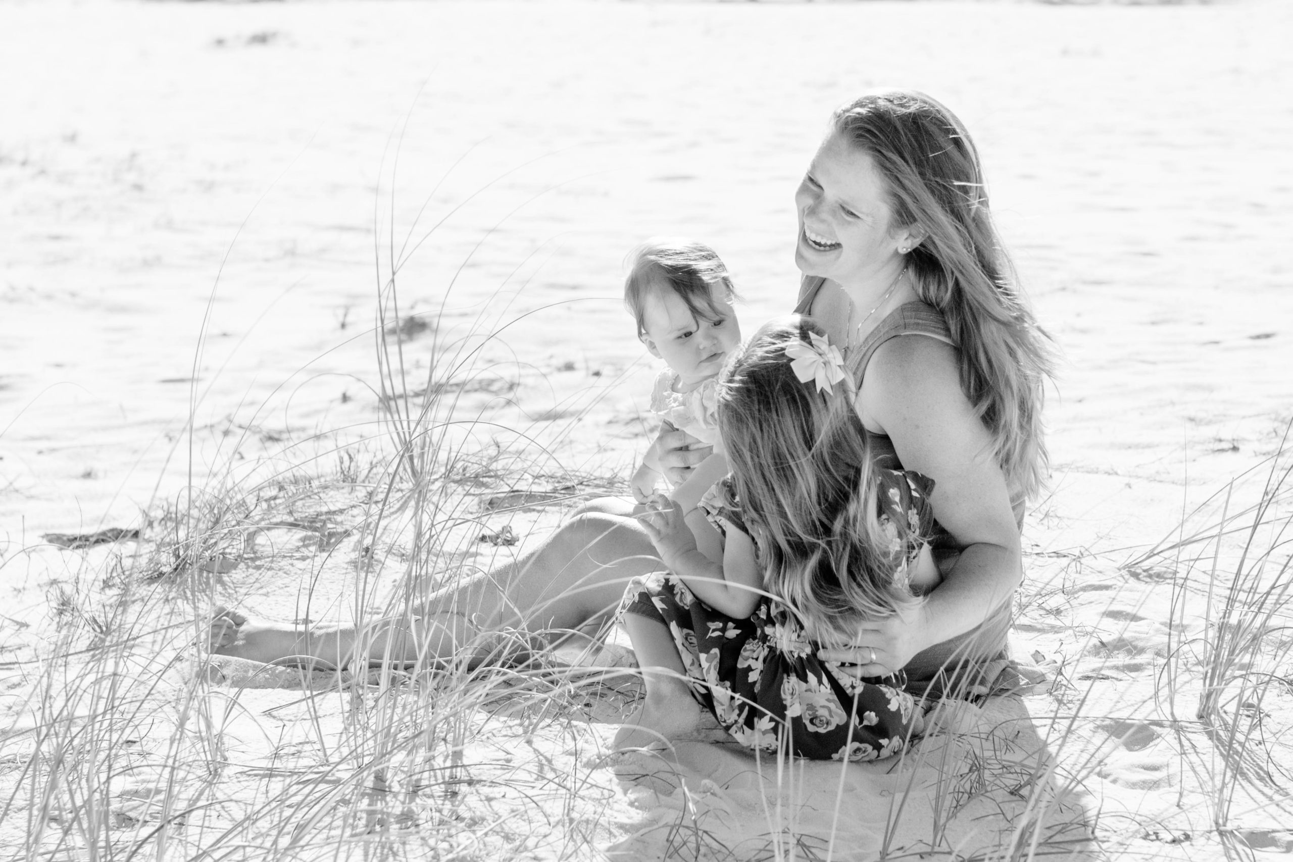 Mother laughing on the beach in Pensacola, FL with her 2 daughters during a family photo session with Jenny Macy Photography