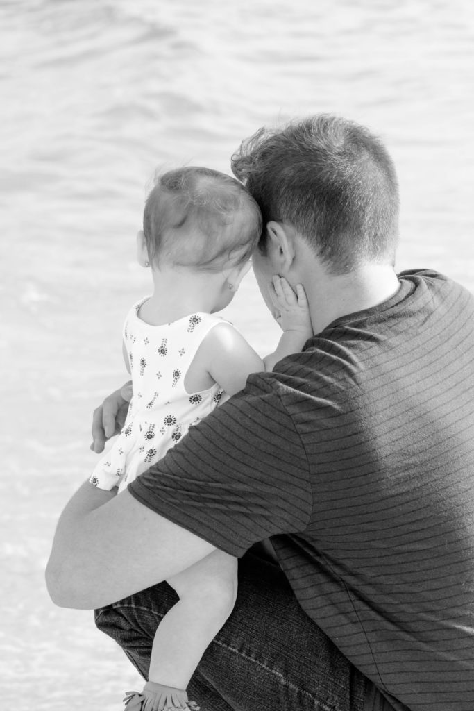 black and white photo of a father looking at the ocean with his baby daughter