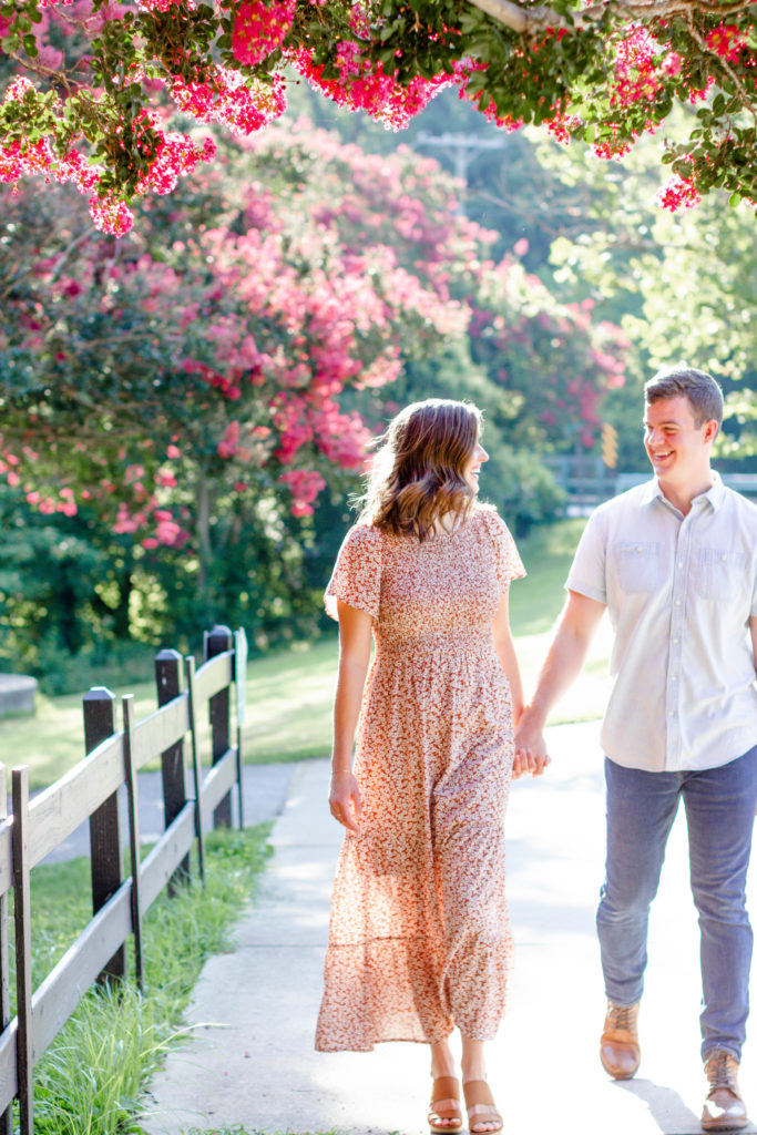 A couple walking down a street with flowers and a fence during a Greenville SC Family Mini Session Maternity Session by Greenville family photographer Jenny Macy Photography
