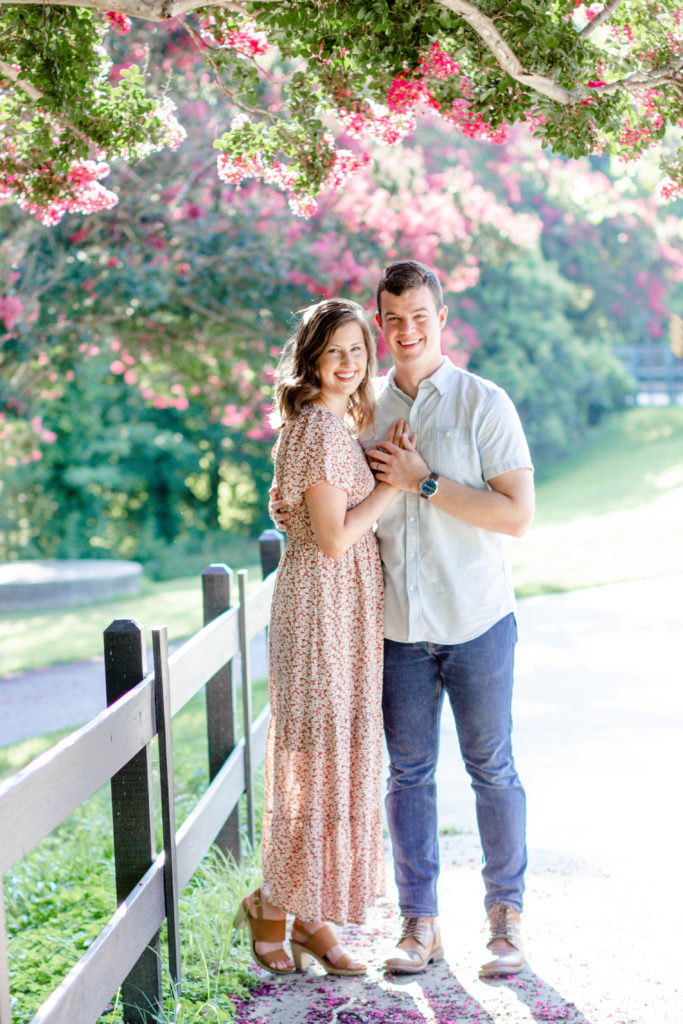 A couple standing along a fence at a park with floral trees during a Greenville SC Family Mini Session Maternity Session by Greenville family photographer Jenny Macy Photography