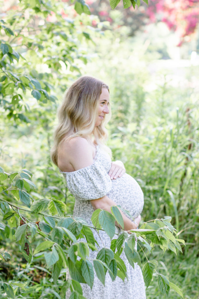 A mom cupping her tummy surrounded by leaves during a maternity mini session and family mini session in Greenville, SC by Jenny Macy Photography.
