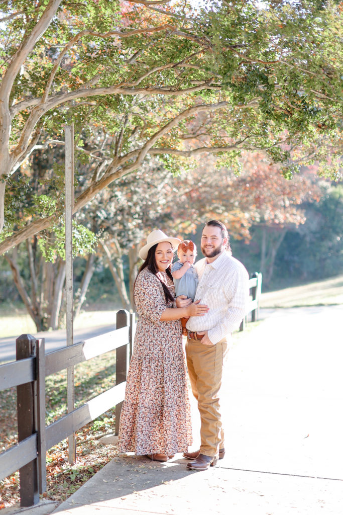 A family by a fence during a Greenville, SC fall mini session with Jenny Macy Photography.