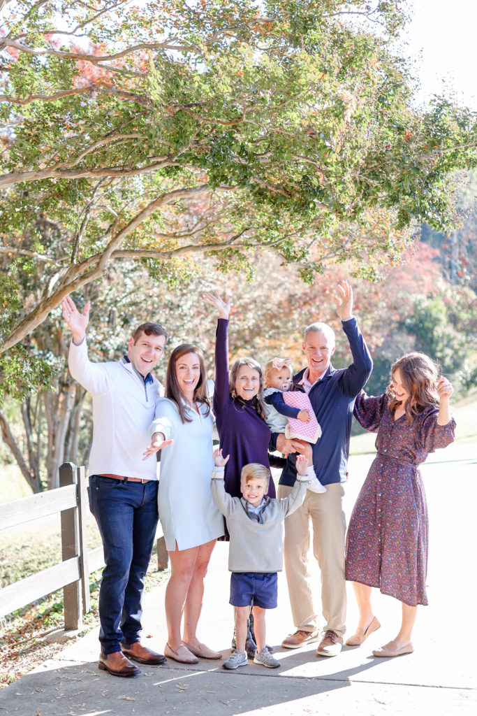 An extended family laughing and throwing their hands up during a fall family photo session in Greenville, SC with Jenny Macy Photography.