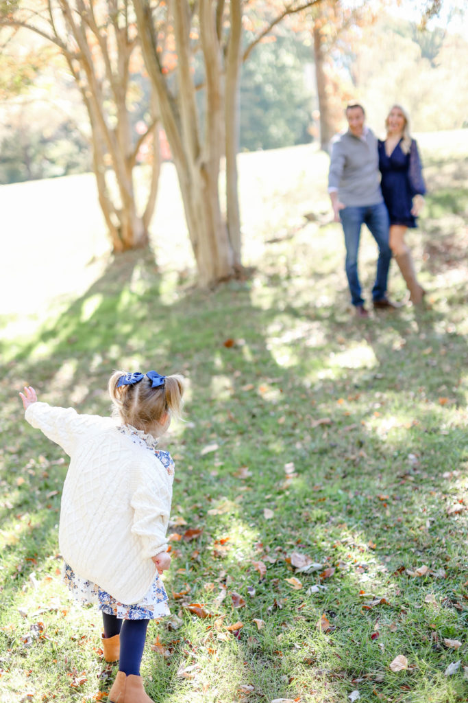 A little girl running up to her mom and dad during a fall family session in Greenville, SC by Jenny Macy Photography.