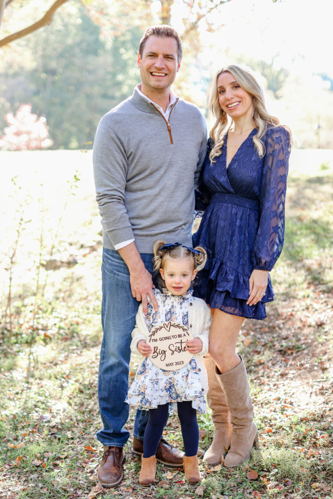 A little girl holing a pregnancy announcement during a fall family session in Greenville, SC by Jenny Macy Photography.