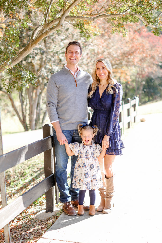 A family of 3 by a fence during a fall family session in Greenville, SC by Jenny Macy Photography.