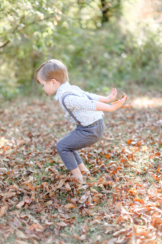 A little boy in suspenders jumping in leaves during a fall mini session in Greenville, SC with Jenny Macy Photography.