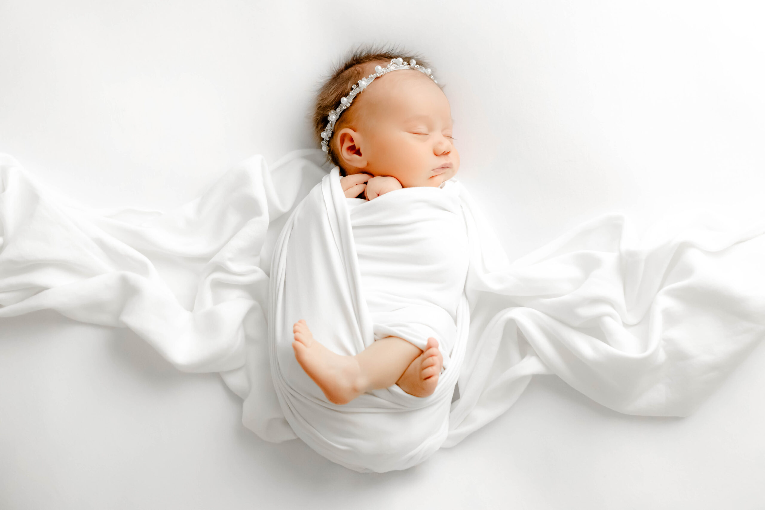 A sleeping baby swaddled in a white blanket during a newborn photo session in greenville, SC